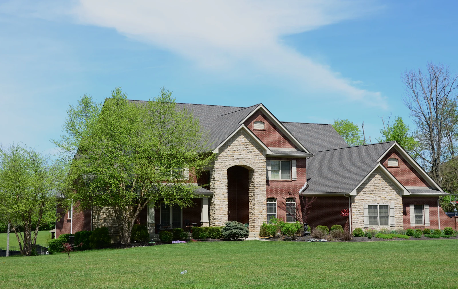 Two-story brick family home with a green front lawn under a blue sky